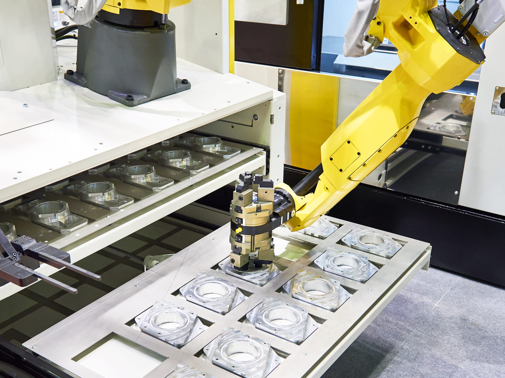 robotic arm with precision gripper transferring machined metal components between conveyor trays in a flexible manufacturing cell designed for quick retooling and model changeovers