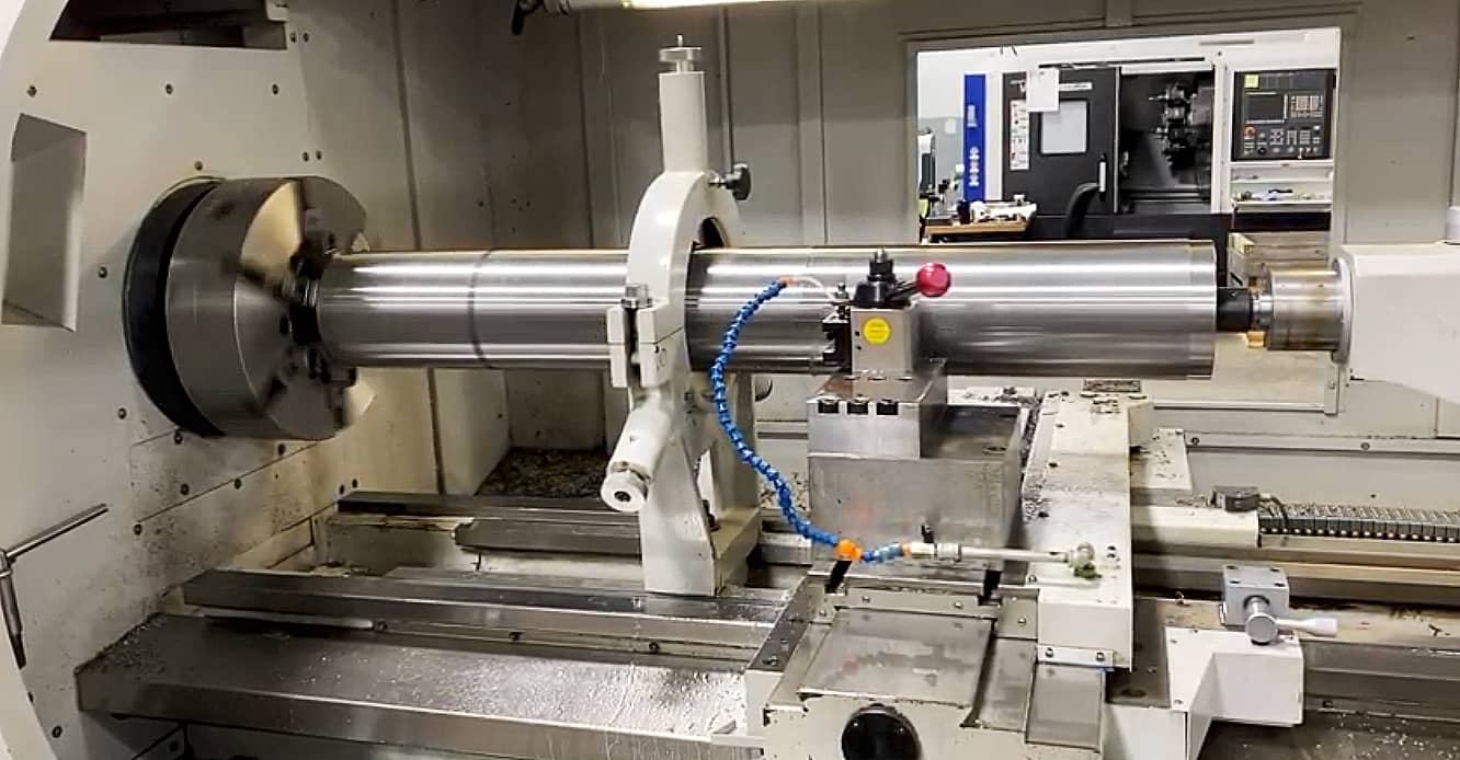 large industrial roll mounted inside a precision machining lathe during shaft and tooling restoration work for tire and calendering production equipment