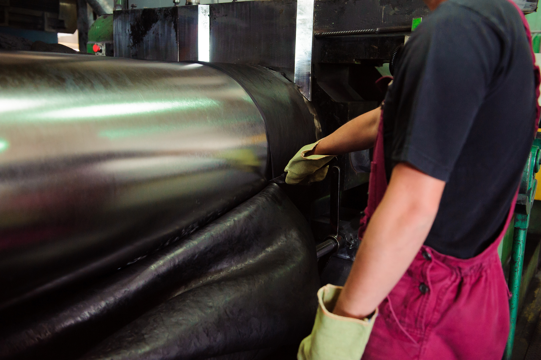 industrial worker monitoring rubber material passing through large calender rollers, illustrating how mechanical deviation, roll wear, and shaft misalignment create instability and variation in manufacturing processes