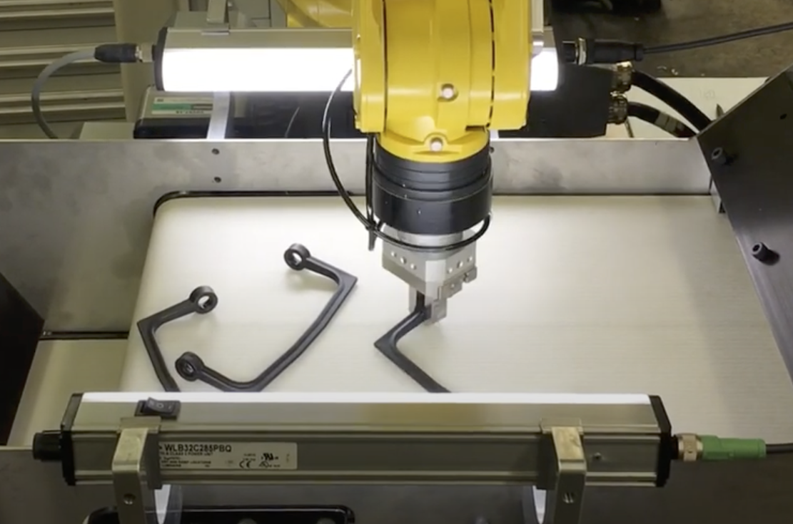 an automated robotic arm picking automotive parts from a conveyor belt feeder